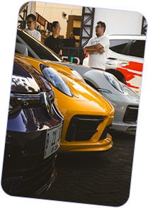 Front view of a row of luxury sports cars in black, yellow, and silver colors with three people standing and talking in the background.